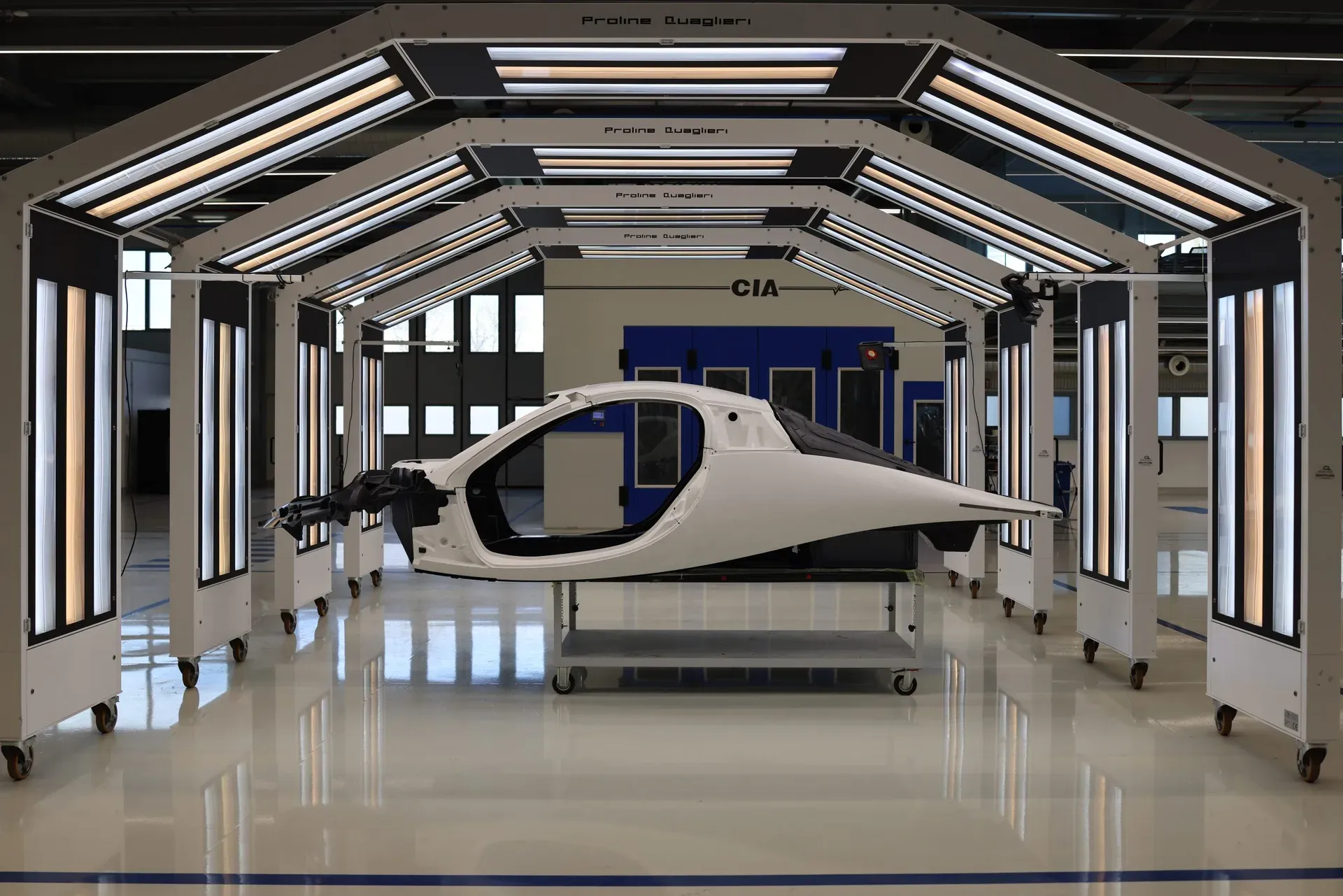 An Aptera vehicle body shell on a stand under inspection lights in a factory